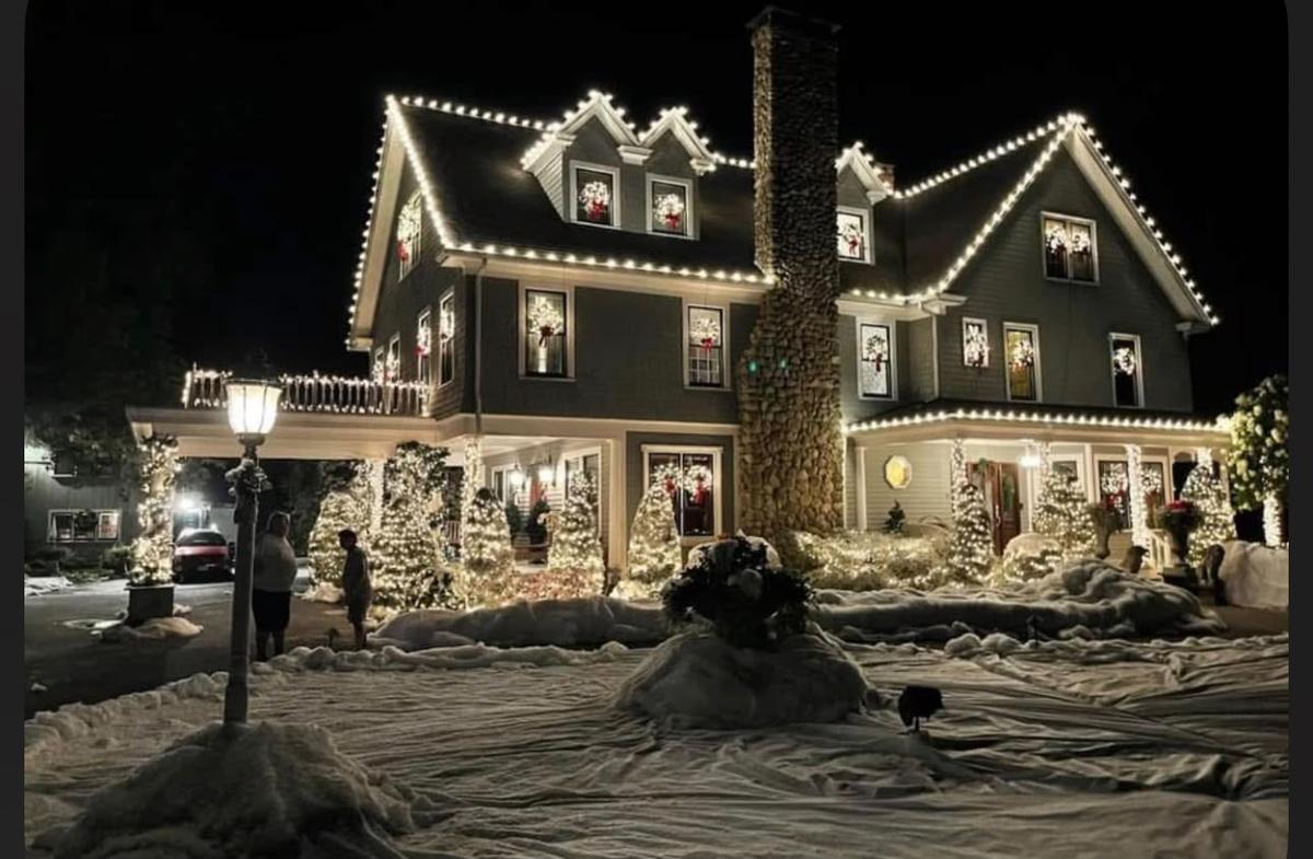 Two-story home with warm white roofline lights and wrapped trees